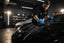 Professional detailer applying ceramic coating to a black car hood with a microfiber applicator in a dark garage